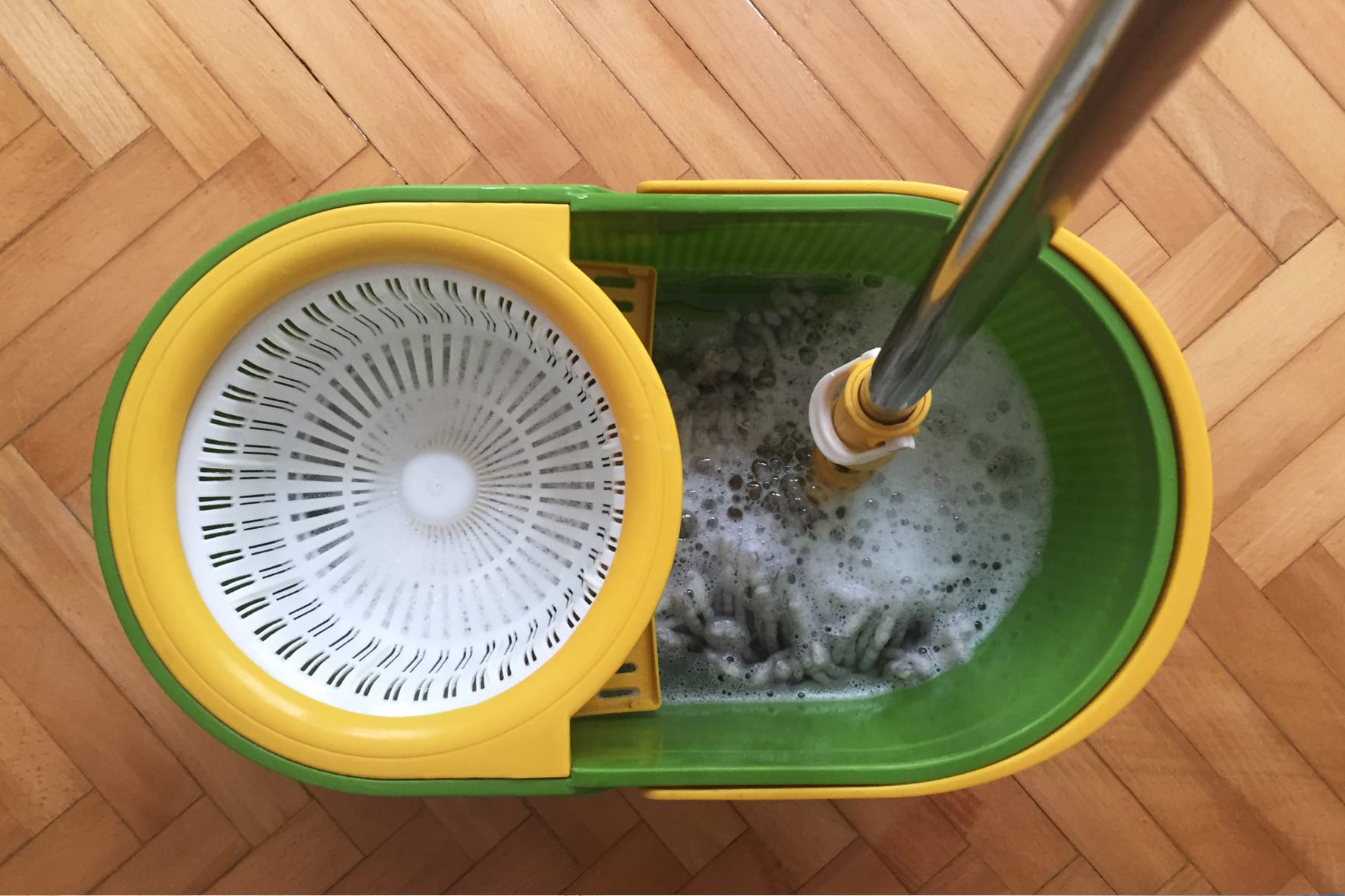 Emmer met zeepsop en een mop op een eiken visgraatvloer tijdens het dagelijkse onderhoud