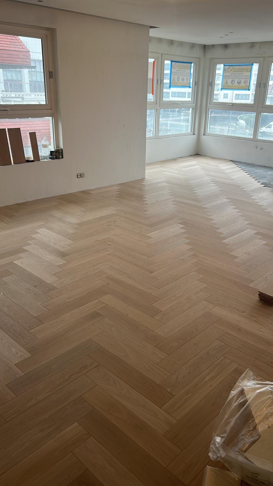 Pas gelegde eiken visgraatvloer in een lichte woonkamer, de laatste planken liggen nog klaar