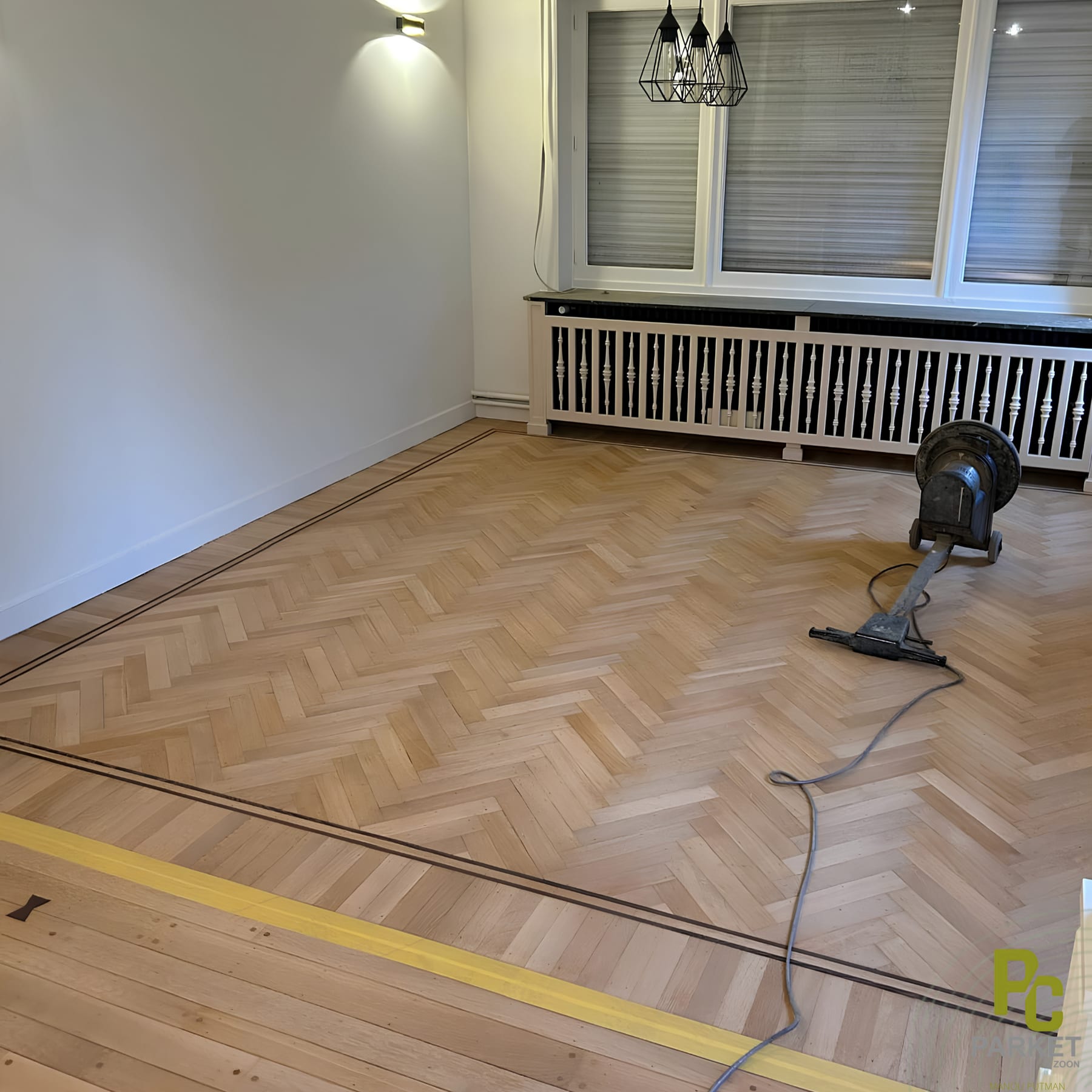 Oude eiken visgraatvloer met sierlijst die halverwege het schuren staat, de schuurmachine staat nog op de vloer