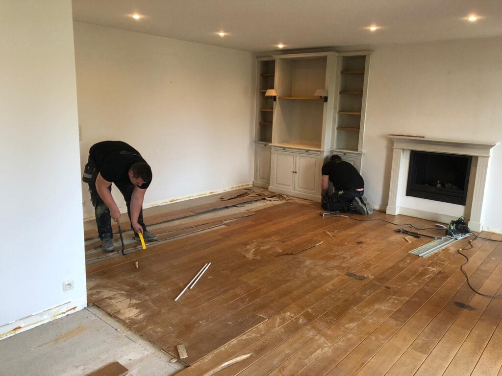 Twee vakmensen aan het werk bij de renovatie van een eiken plankenvloer in een woonkamer